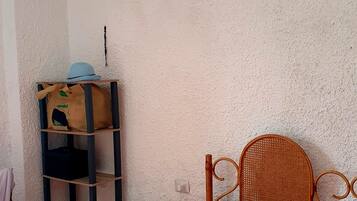 Una camera da letto con un letto, uno scaffale con una borsa, una sedia e un condizionatore d'aria.