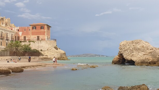 A coastal building with a stone facade and a red-tiled roof overlooking a beach with clear turquoise water and rocky formations. - Mini apartment "CirPi" (max 4 people) Desusino near the sea (Butera)