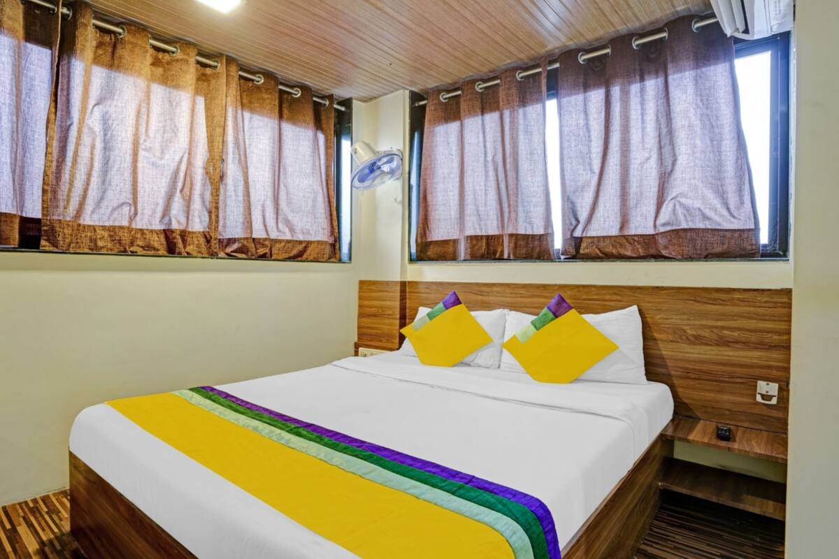 A hotel room with a wooden headboard, a bed with a white and yellow striped bedspread, and curtains on the windows.