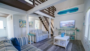 A living room with striped sofas, a television, a staircase, and a surfboard decoration.