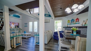 A spacious living area with a high ceiling, a dining table with chairs, a sofa, and a TV.