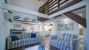 A spacious living area with striped sofas, a white coffee table, and a staircase leading to an upper level.