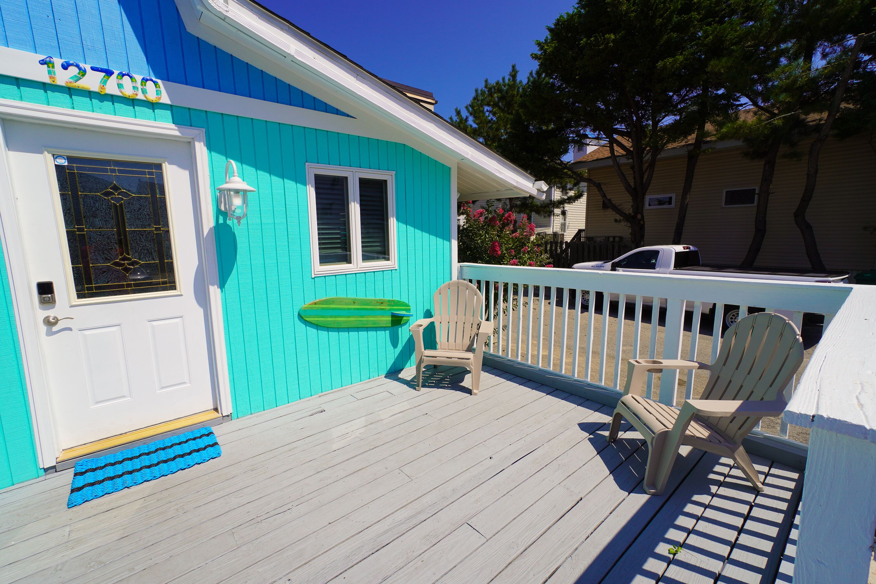 A turquoise house with a white door, a window, and a porch with two Adirondack chairs.