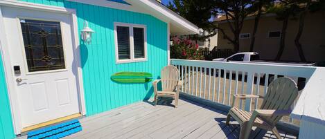 A turquoise house with a white door, a window, and a porch with two Adirondack chairs.
