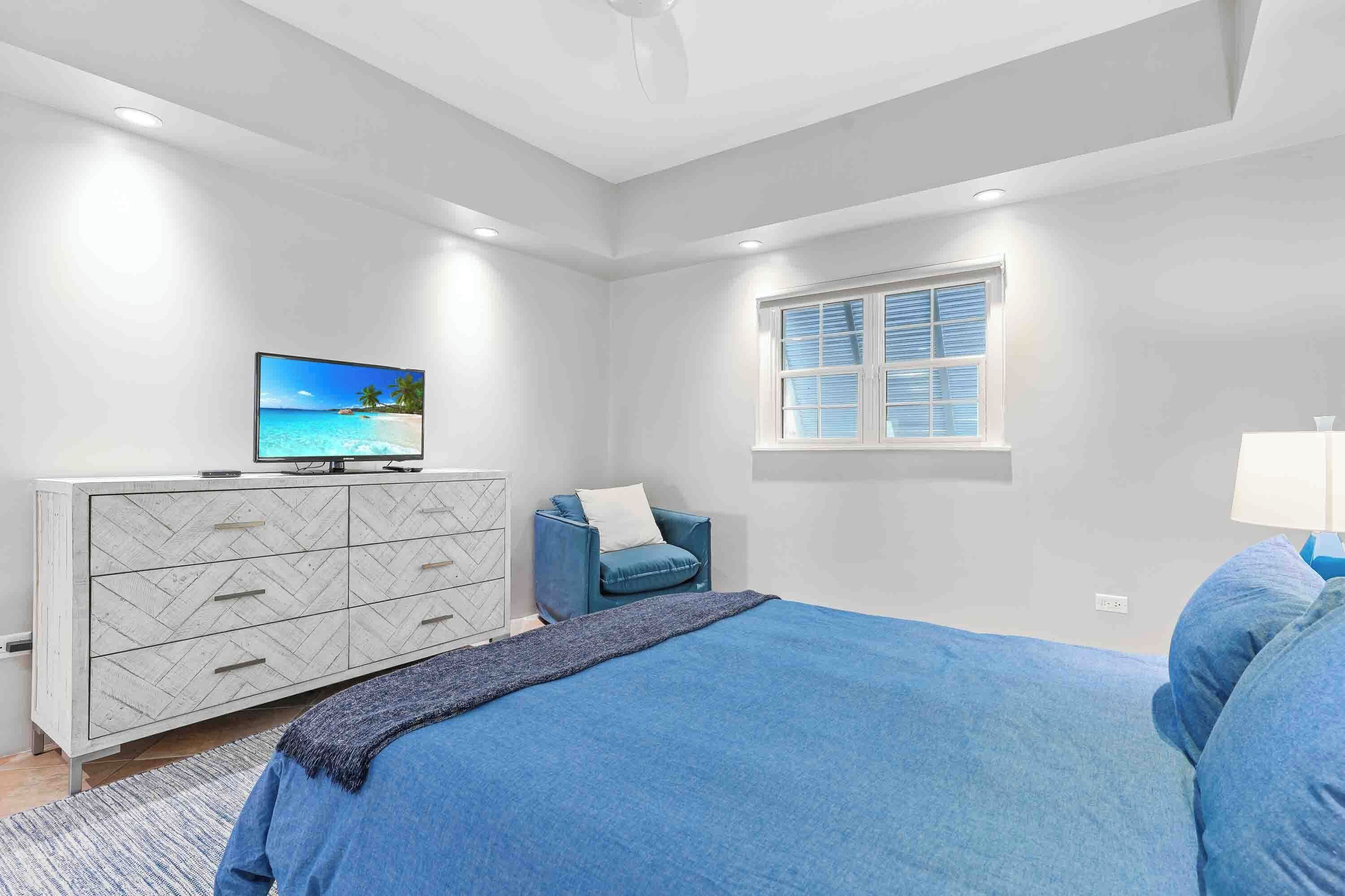 Une chambre à coucher avec un lit, un téléviseur posé sur une commode, une fenêtre et une chaise.