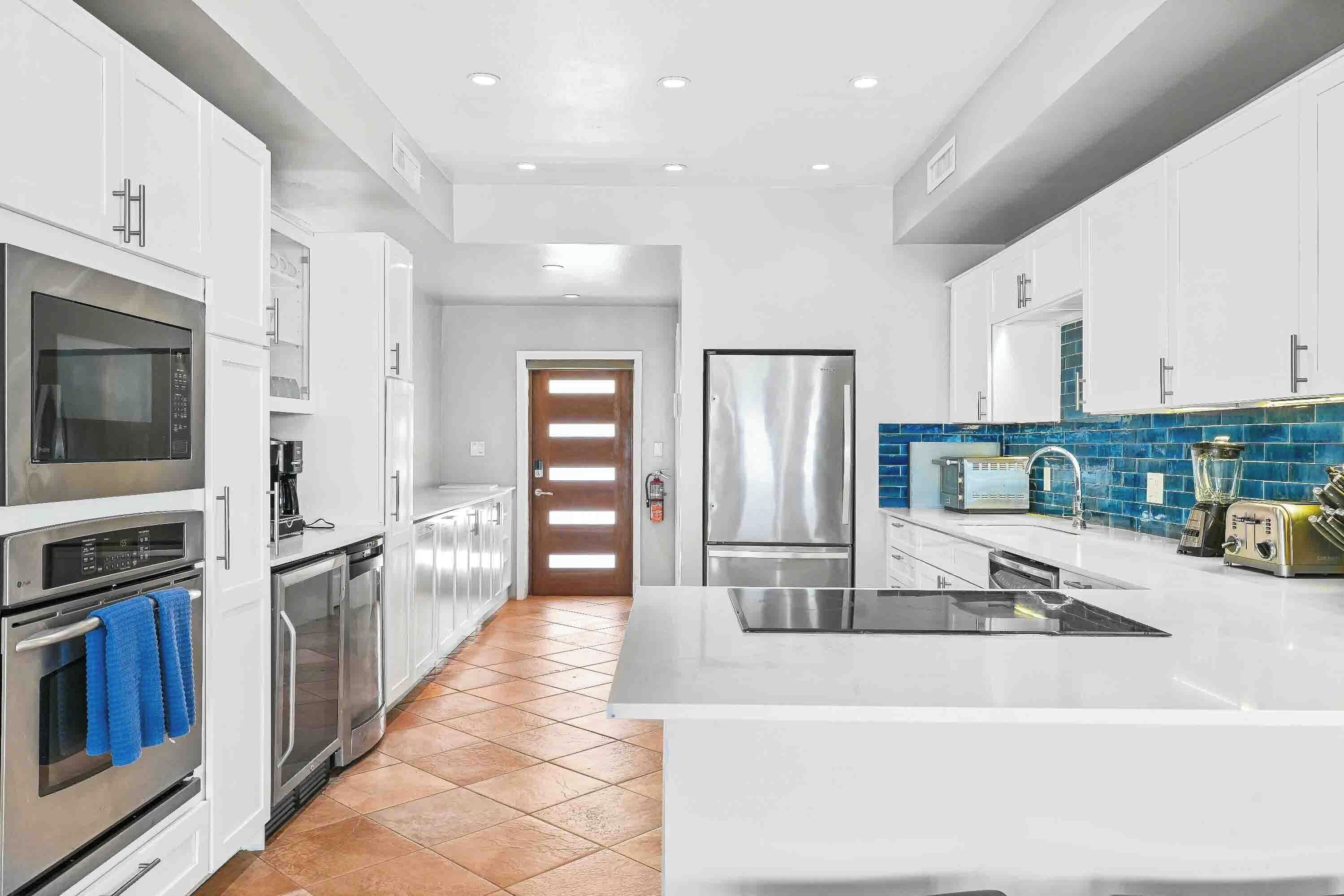 A modern kitchen with white cabinets, stainless steel appliances, and a blue-tiled backsplash.