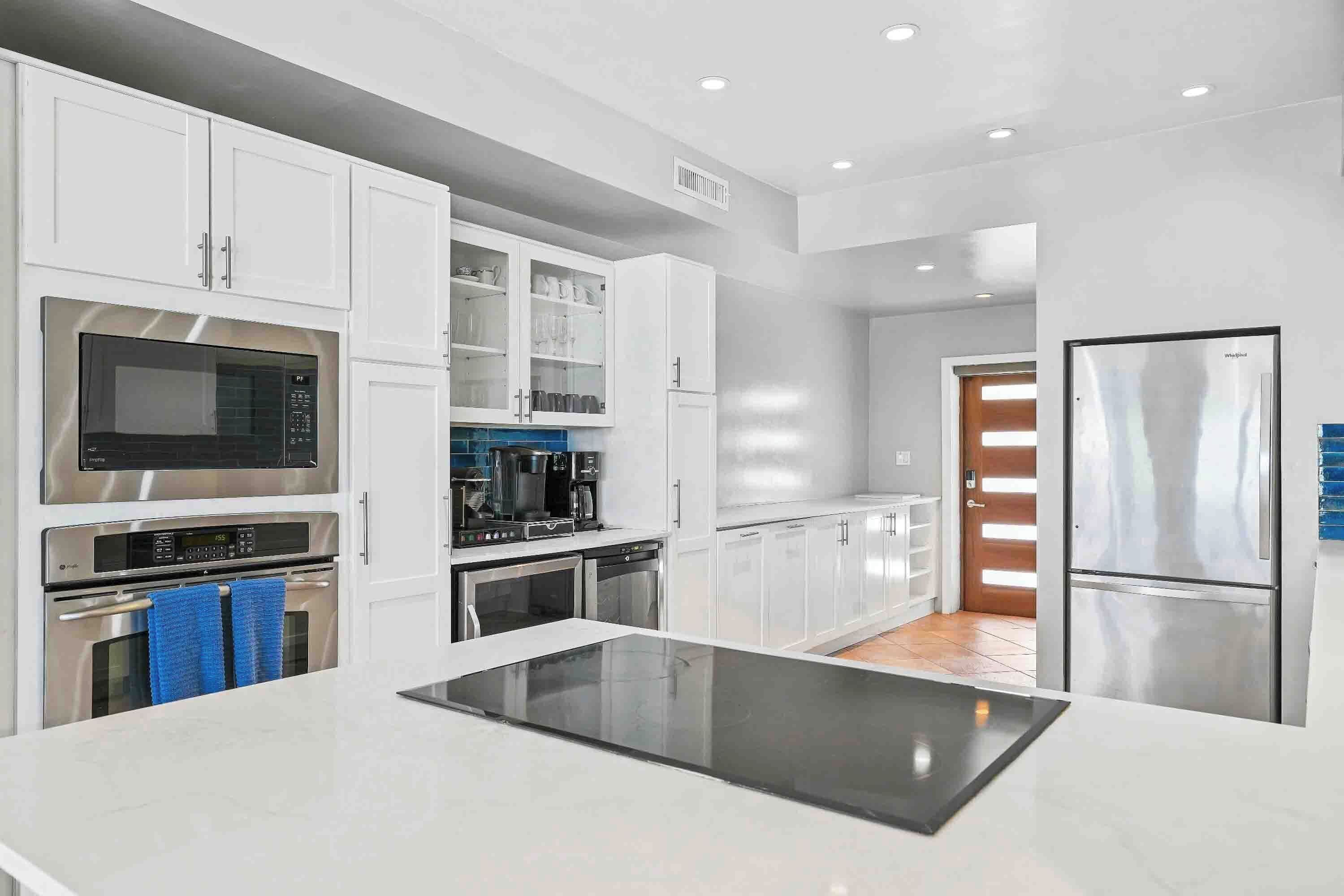 A modern kitchen with white cabinetry, a built-in microwave, a coffee maker, and a stainless steel refrigerator.