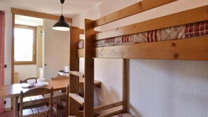 A bunk bed with a wooden frame and a quilted mattress. There is a table with chairs and a hanging light fixture. - 100m from ski slopes, 3rd floor, view ski slopes/ski slopes, balcony, tv, 28m², La Plagne (La Plagne)