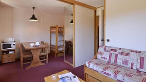 A compact room with a wooden table, a sofa, a bunk bed, a microwave, and a ceiling light. - 100m from ski slopes, 3rd floor, view ski slopes/ski slopes, balcony, tv, 28m², La Plagne (La Plagne)