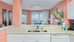 Een keuken met een dubbele spoelbak, witte kasten, een vaatwasser en een groot raam met uitzicht.