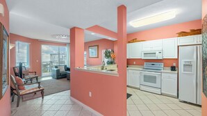 Een moderne keuken met witte kasten, een magnetron, oven en koelkast. Er is een eethoek met gestreepte stoelen en uitzicht op de stad.