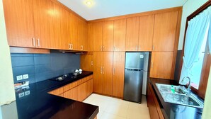 A modern kitchen with wooden cabinets, a stainless steel refrigerator, and a black countertop. - NIL VILLA SEMINYAK - 3 BEDROOMS (Bali)