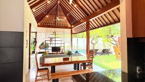 A modern kitchen with a wooden ceiling, a dining area with a table and chairs, and a view of the outdoors. - NIL VILLA SEMINYAK - 3 BEDROOMS (Bali)