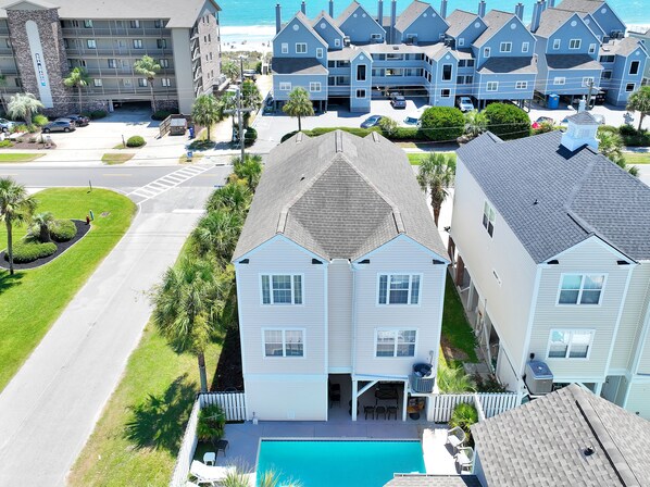 A two-story house with a swimming pool, a covered patio, and a view of the beach.