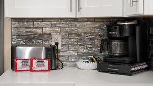 A kitchen with a stone backsplash, a toaster, a coffee maker, and two packets of popcorn.