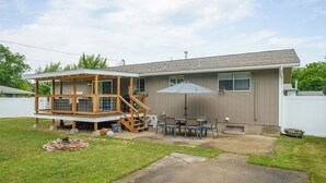 A residential house with a wooden deck, a patio with a table and chairs, and a covered outdoor area.