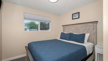 A bedroom with a bed, a window, a headboard, and a small bedside table.