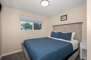 Een slaapkamer met een bed, een raam, een hoofdeinde en een klein nachtkastje.