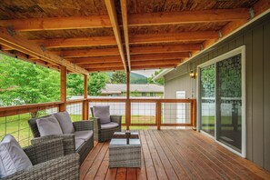 A covered deck with wicker furniture and a glass door leading to a house.