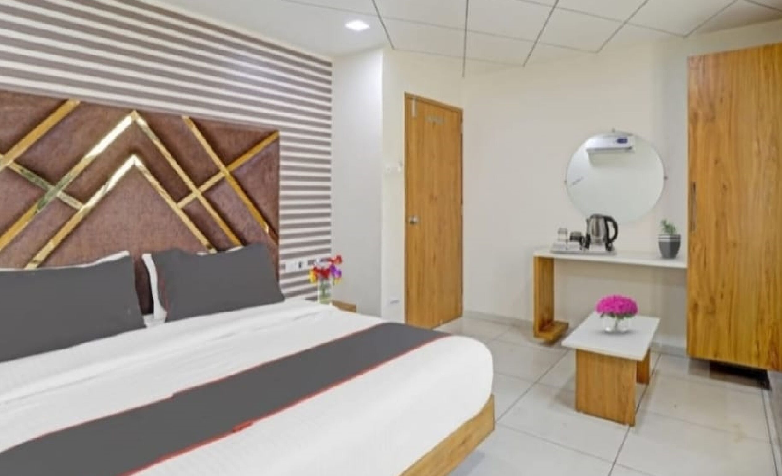Une chambre à coucher moderne avec un grand lit, une tête de lit en bois, une table de chevet avec un miroir et une petite armoire en bois.