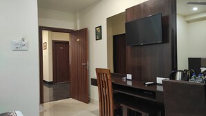 Una habitación de hotel moderna con una mesa de comedor de madera, un televisor montado en la pared y una zona de kitchenette.