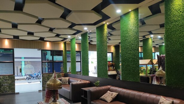 Un lobby moderno con un sofá de cuero marrón, una mesita con un objeto decorativo y paneles verticales verdes.