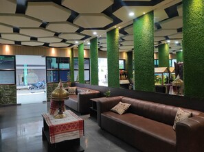 A modern lobby with a brown leather sofa, a small table with a decorative item, and green vertical panels. - Hotel Paradise (Biswanath)