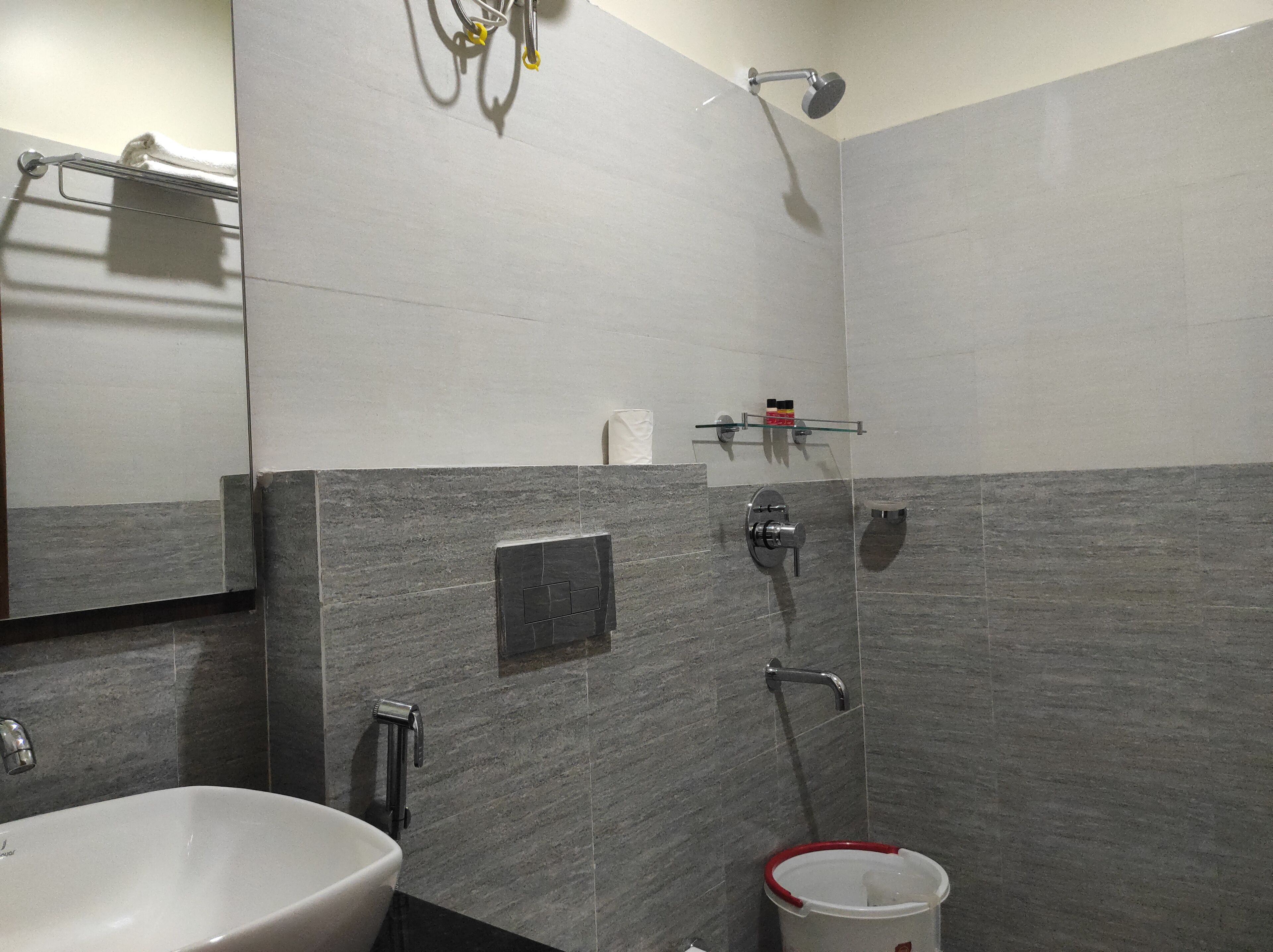 Un baño con lavamanos blanco, ducha con cabezal de ducha manual, toallero y dispensador de papel higiénico en la pared.