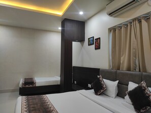 Habitación de hotel con una cama grande, una cama más pequeña, un cabecero oscuro, un aire acondicionado instalado en la pared y dos cuadros enmarcados.