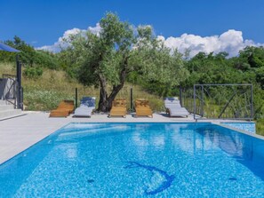 Ein Swimmingpool mit klarem, blauem Wasser, umgeben von Holzliegen und einem Baum.