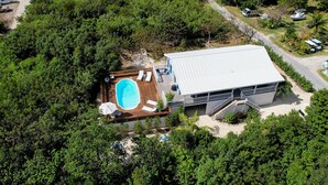 Vista aérea de una propiedad con piscina, sillas de deck y un edificio grande con techo de metal.