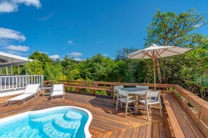 A wooden deck with a hot tub, outdoor seating, and a view of lush greenery. - Elbow Joint: Comfortable Island Escape in White Sound near Firefly Resort (Hope Town)