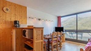 Een gezellige kamer met houten wanden, een eethoek met stoelen, een televisie en een groot raam met uitzicht op heuvels.