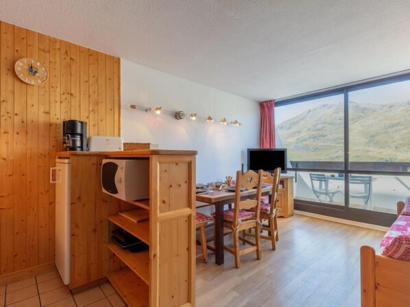 A cozy room with wooden walls, a dining area with chairs, a television, and a large window with a view of hills.