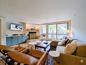 A living room with a fireplace, a television, a sofa, and a view of the outdoors.
