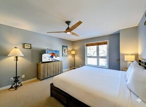 A bedroom with a bed, ceiling fan, TV, and two lamps.