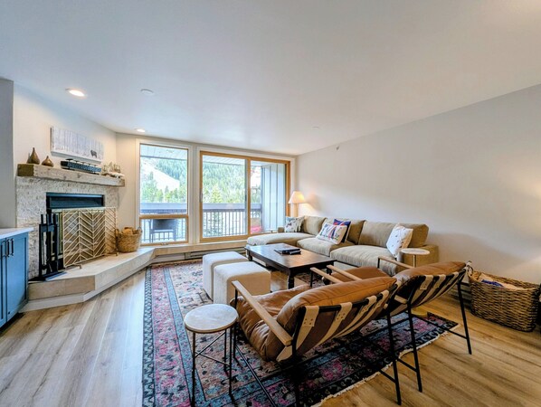 A spacious living room with a fireplace, large windows, a sofa, and a coffee table.
