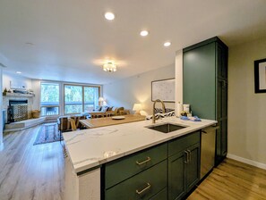 A modern kitchen with a large island, built-in green cabinets, and a fireplace.