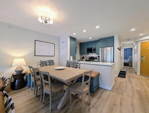 A modern kitchen with a central island, a dining area with a table and chairs, and a hallway leading to a bedroom.
