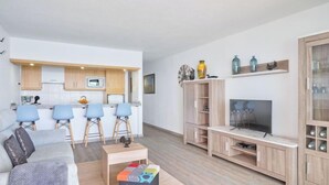 Un soggiorno moderno con un divano, un tavolino da caffè e una televisione. È presente una zona cucina con un forno a microonde e un lavandino.