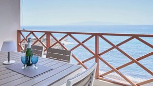 Un tavolo di legno con due bicchieri blu e una bottiglia, con vista su una spiaggia e una ringhiera in legno.