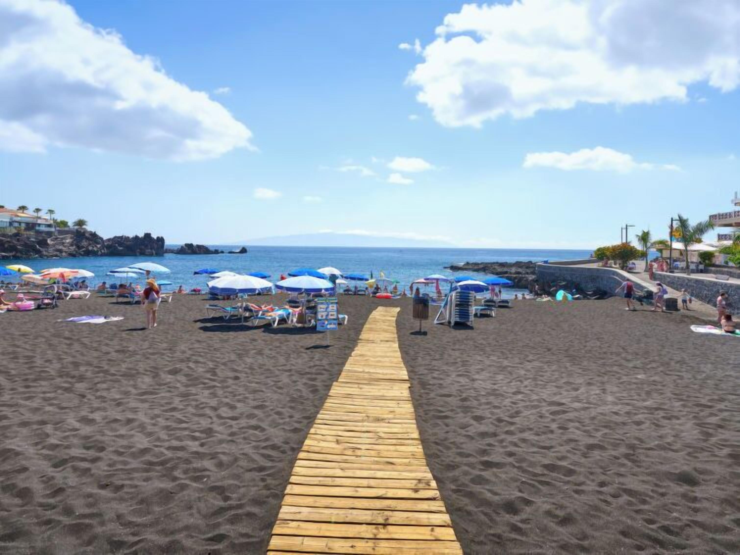 A sandy beach with a wooden walkway leading to the water, umbrellas, and beach chairs.