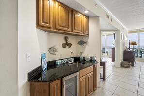 A kitchen with wooden cabinets, a black countertop, and a dishwasher. There are decorative items on the wall and a sign indicating a beach view. - The Colonnades 1002 by Liquid Life (Gulf Shores)