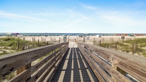 A wooden boardwalk leading to a beach with umbrellas and beachgoers. - The Colonnades 1002 by Liquid Life (Gulf Shores)