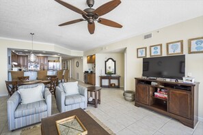 A spacious living room with a large TV, comfortable seating, and a dining area with wooden furniture.