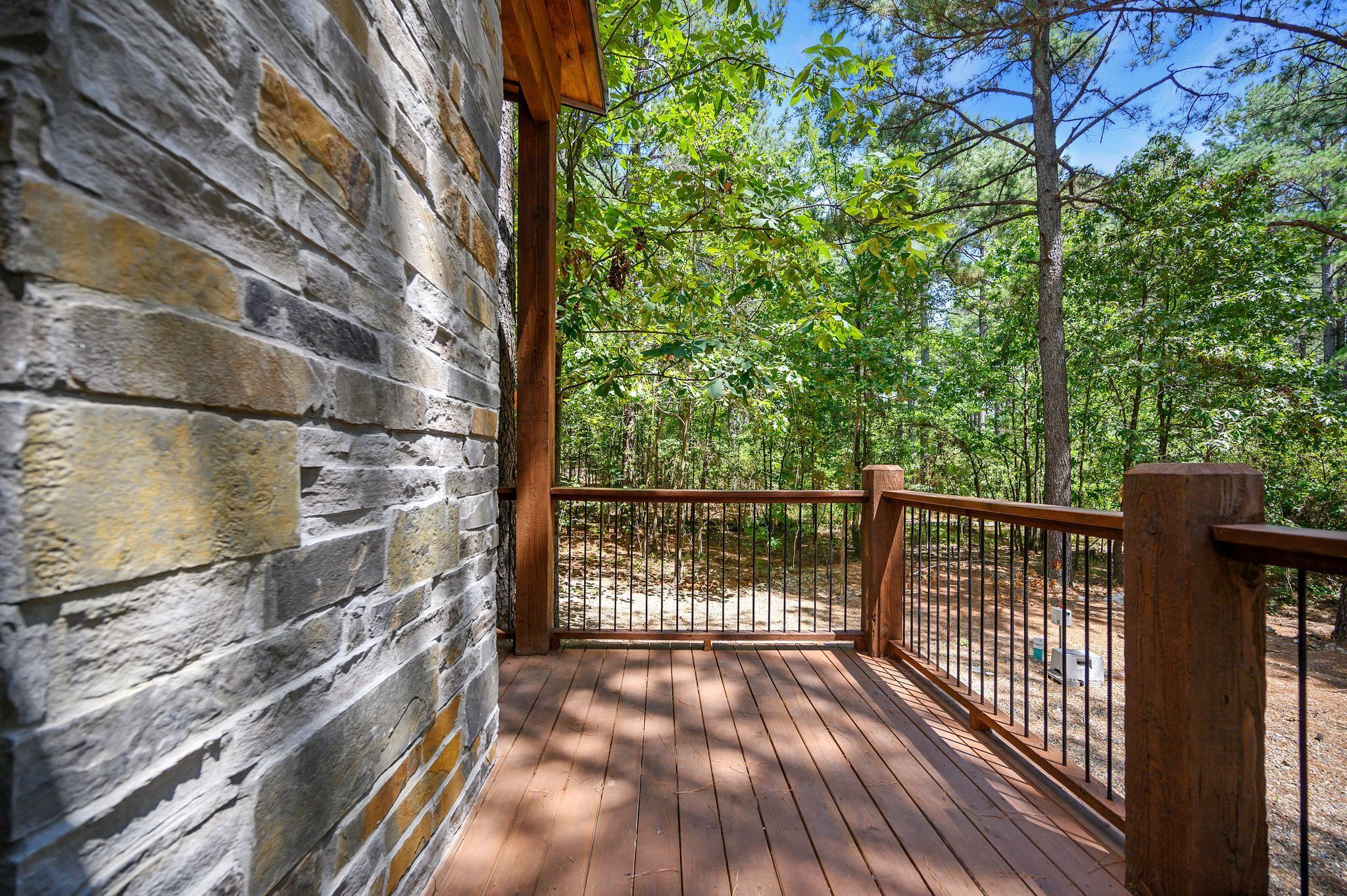 A wooden deck with a stone wall, surrounded by a forest.