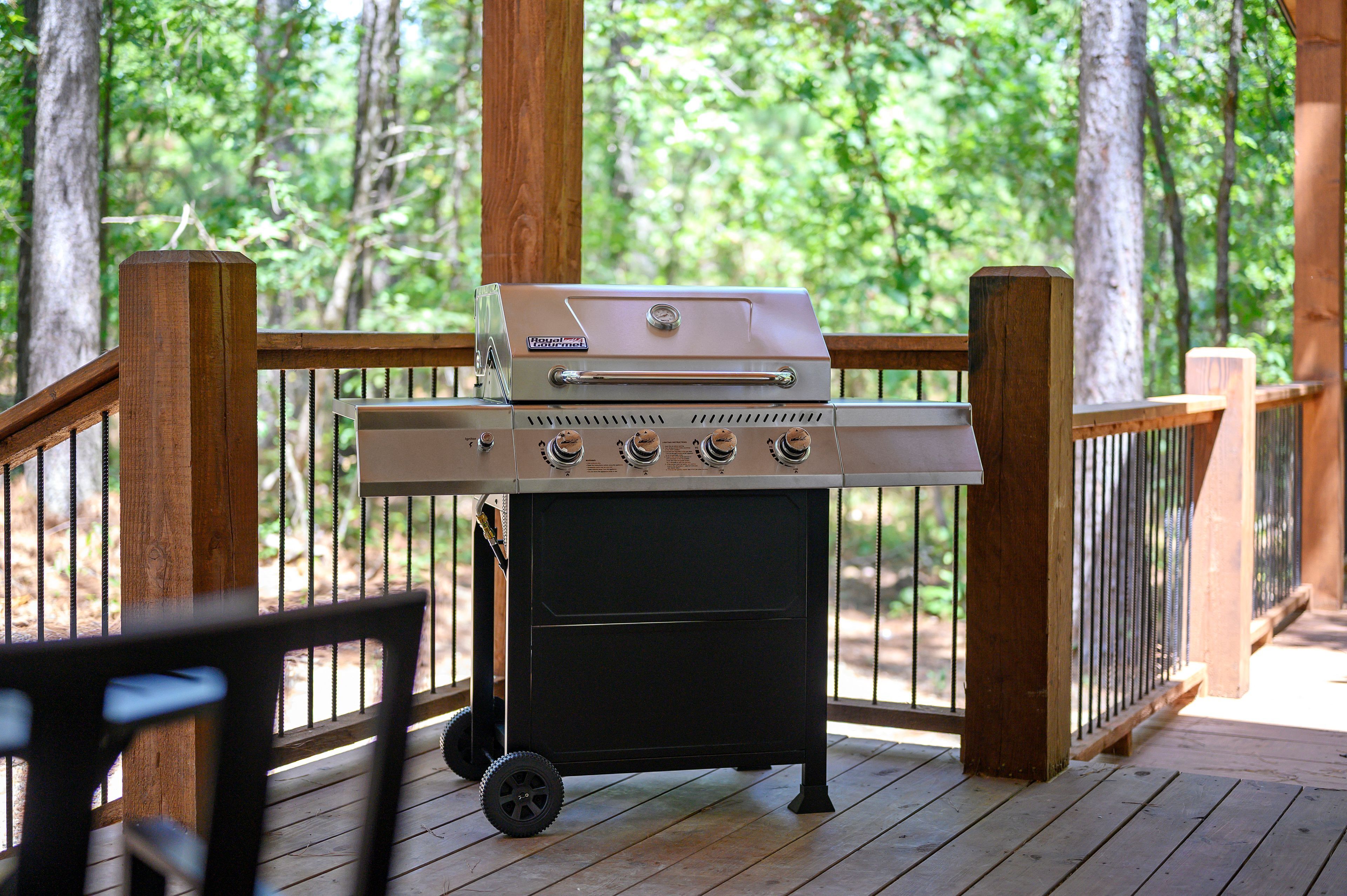 Un barbecue portable sur une terrasse en bois dotée d’une rambarde, entouré d’arbres.