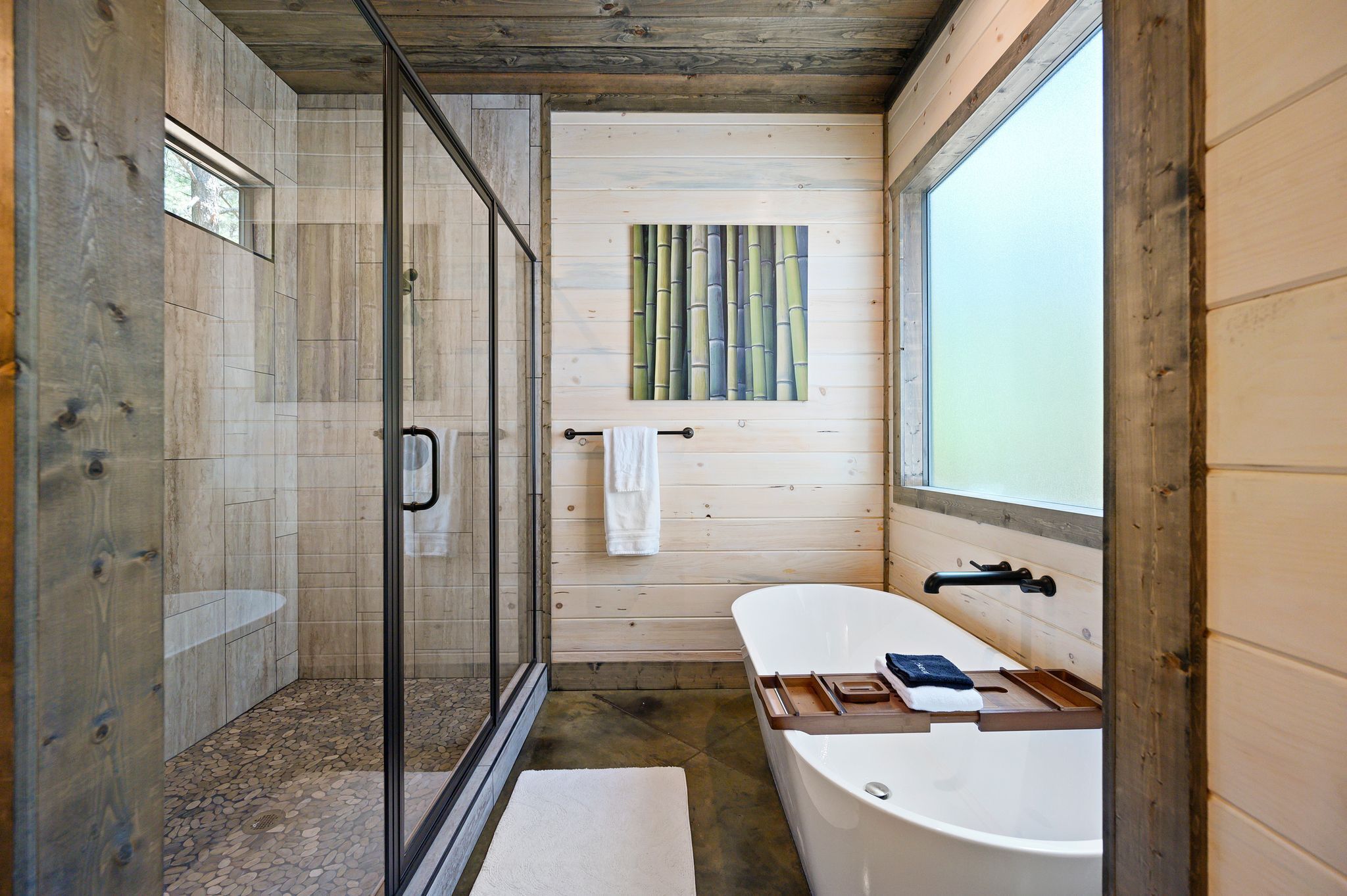 A modern bathroom with a glass-enclosed shower, a freestanding bathtub, and a wooden wall with a bamboo artwork.