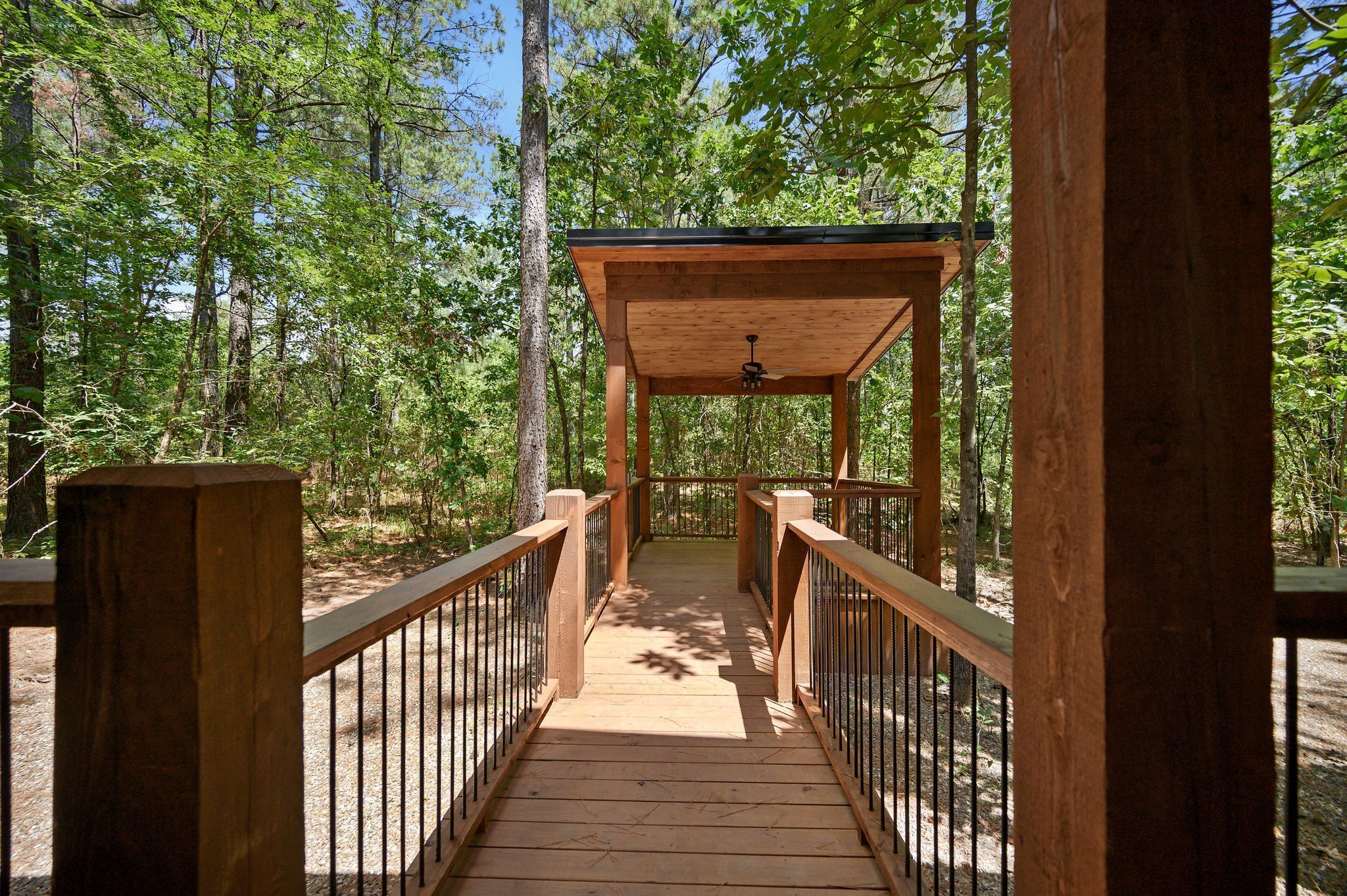 A wooden bridge leading to a covered pavilion in a forested area.