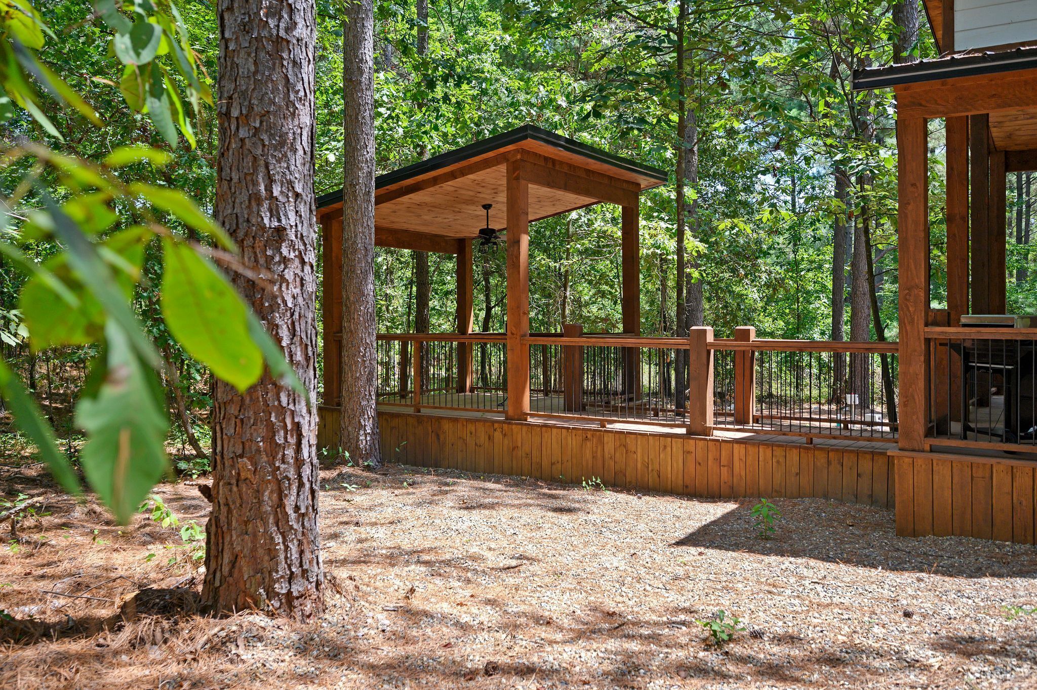 A wooden deck with a covered seating area, surrounded by trees.